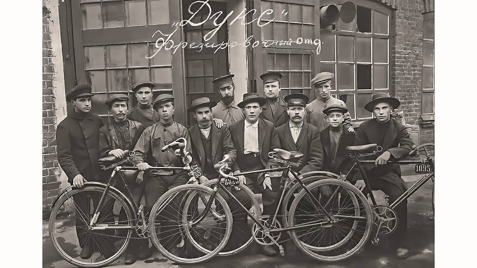 Мастера и рабочие фрезеровочного цеха завода «Дукс» в 1913 или 1914 году. Некоторые – со своими велосипедами, наверное, марки «Дукс». Дату снимка можно определить по номерным знакам, выдаваемым каждую весну сроком на один год