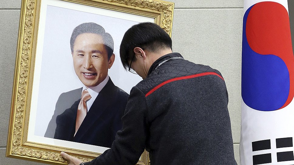 Рабочий снимает портрет бывшего президента Южной Кореи Ли Мён Бака