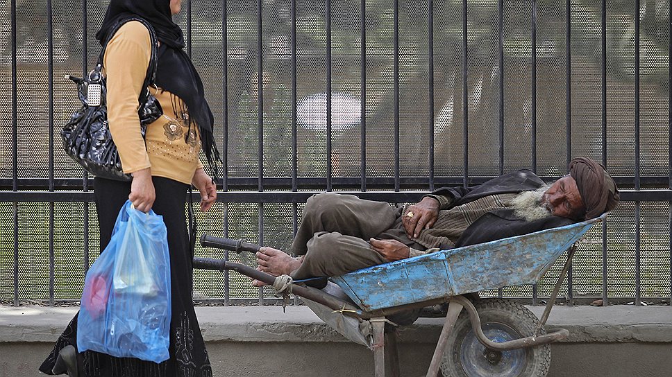 Женщина идет мимо спящего в тачке мужчины в Кабуле (Афганистан), май 2012 года