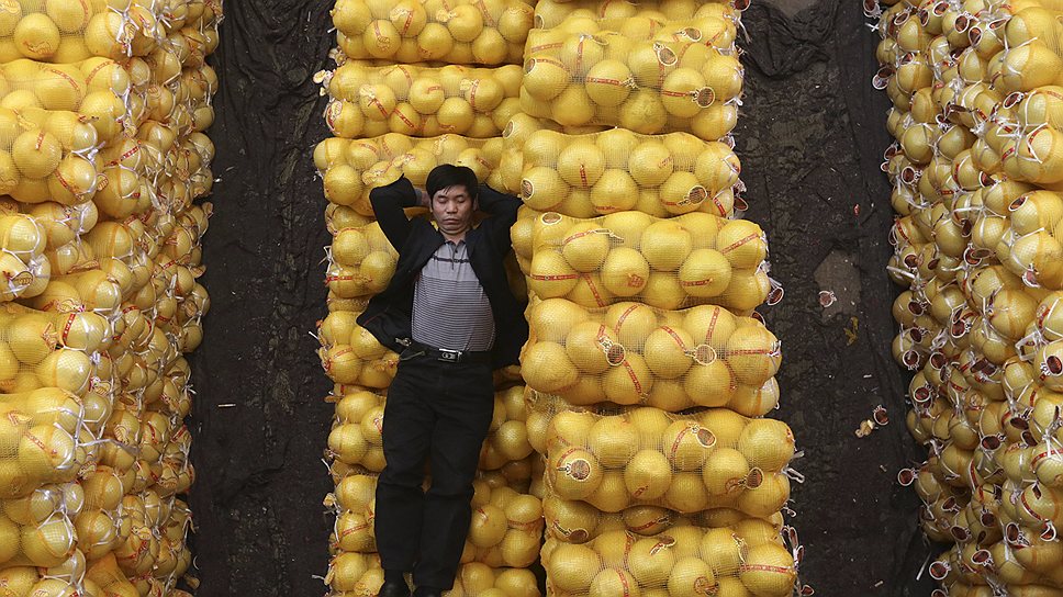 Продавец на мешках с грейпфрутами на продуктовом рынке в городе Ухань (Китай), октябрь 2012 года