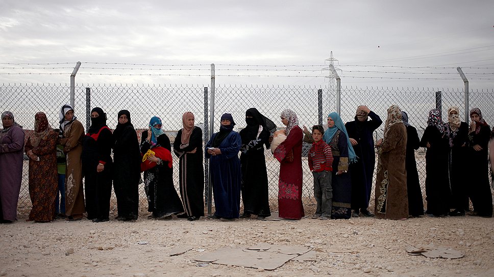 Сирийские женщины стоят в очереди, чтобы получить долю зимних комплектов помощи в лагере беженцев около сирийской границы в Иордании 
