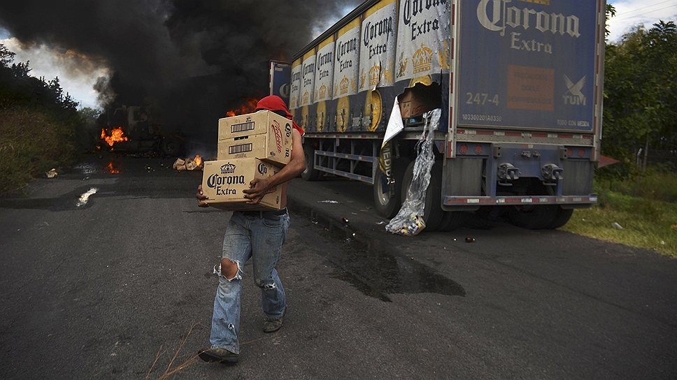 Мексиканские мародеры выносят ящики с пивом Corona из грузовика, загоревшегося в дорожном заторе, который, возможно, устроили местные боевики — тамплиеры