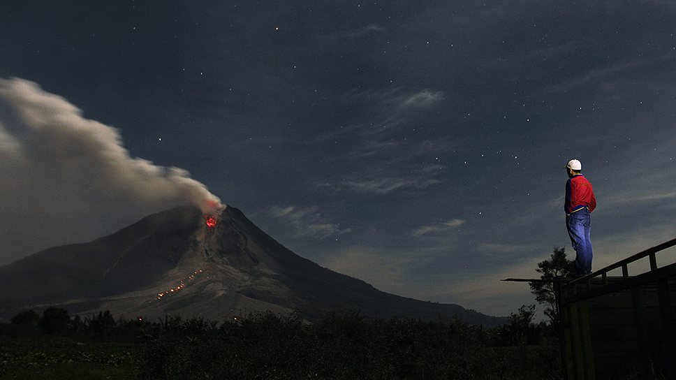 Мужчина наблюдает за извержением вулкана Синабунг на Суматре
