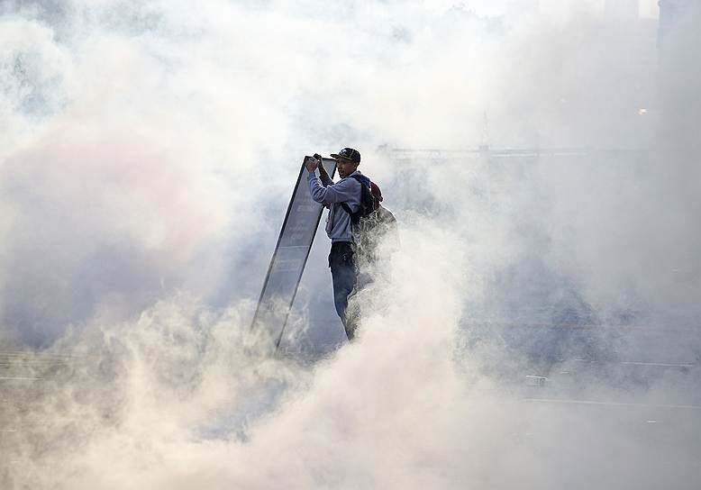 Демонстратор в облаке слезоточивого газа, примененного для разгона акции протеста против правительства Николаса Мадуро в Каракасе