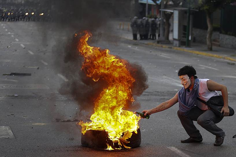 Демонстратор поджигает &quot;коктейль Молотова&quot; от горящей шины во время антиправительственных протестов в Каракасе