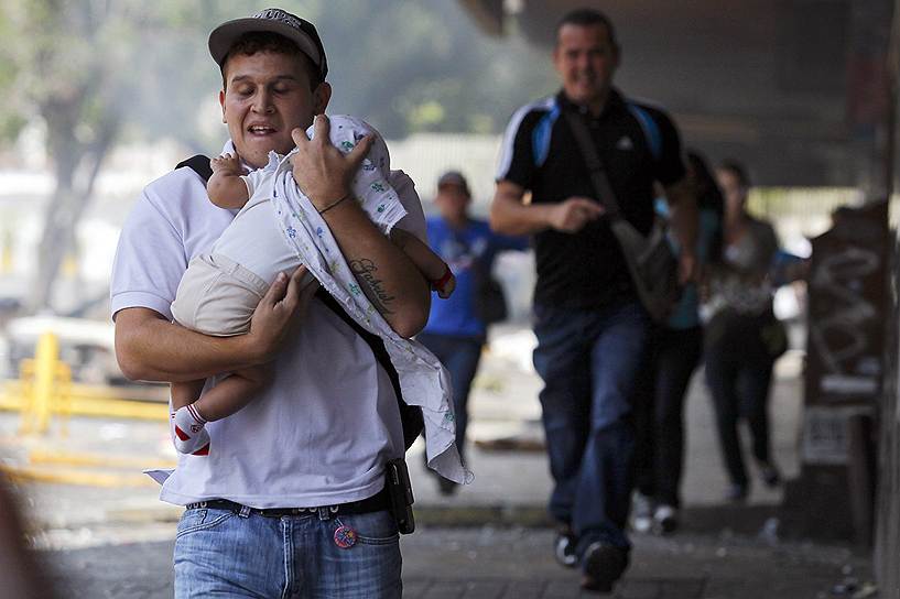 Мужчина с ребенком, убегающий от столкновения сторонников оппозиции с полицией в Каракасе, во время которого был применен слезоточивый газ