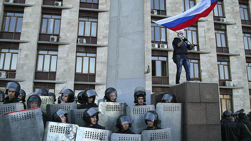 Несколько десятков сотрудников спецназа, вооруженных автоматами Калашникова, без каких-либо опознавательных знаков, одетые в черную форму и в масках, стоят у центрального входа