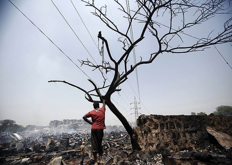 Местный житель смотрит на последствия пожара, уничтожившего сотни лачуг в трущобном районе Нью-Дели
