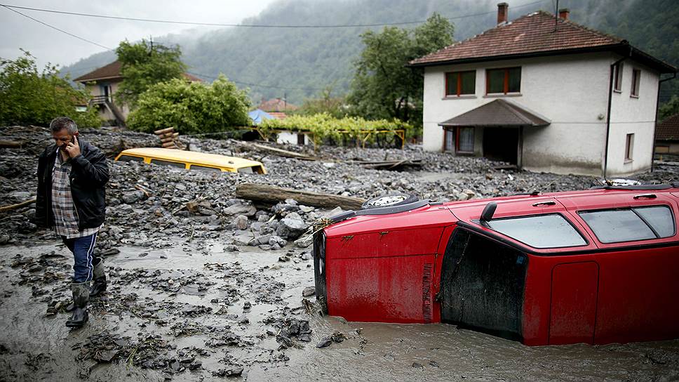 Мужчина возле перевернутого автомобиля, пострадавшего в результате наводнения, Босния и Герцеговина