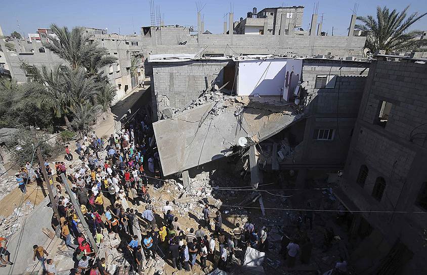 Палестинцы собрались вокруг дома, разрушенного, по данным полиции, в результате бомбардировок израильских ВВС на юге сектора Газа 