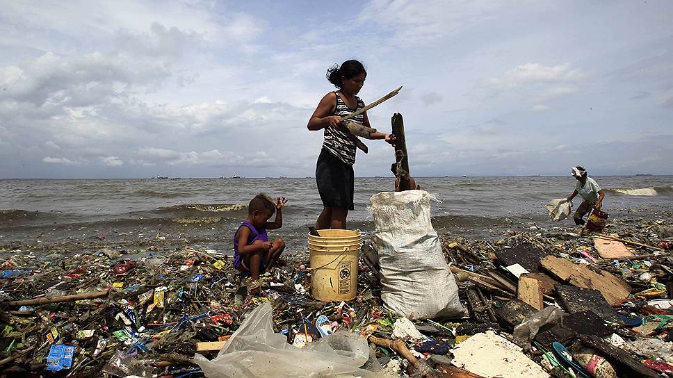 Мать и ребенок собирают перерабатываемые отходы, выброшенные на берег залива в Маниле, Филиппины