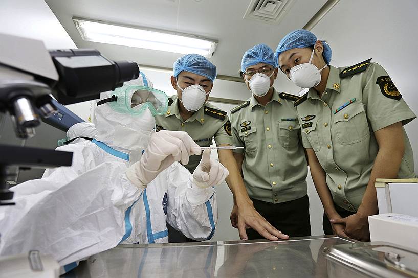 По причине быстрого распространения вируса Эбола китайское правительство отправило странам Западной Африки срочную гуманитарную помощь в размере 30 млн юаней&lt;br> На фото: представитель санитарного контроля (слева) демонстрирует сотрудникам таможни аэропорта Циндао, Китай, симптомы вируса Эбола