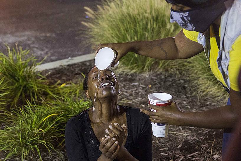 Американские демонстранты промывают глаза после слезоточивого газа, примененного полицией для разгона акции протеста в Фергюсоне, штат Миссури