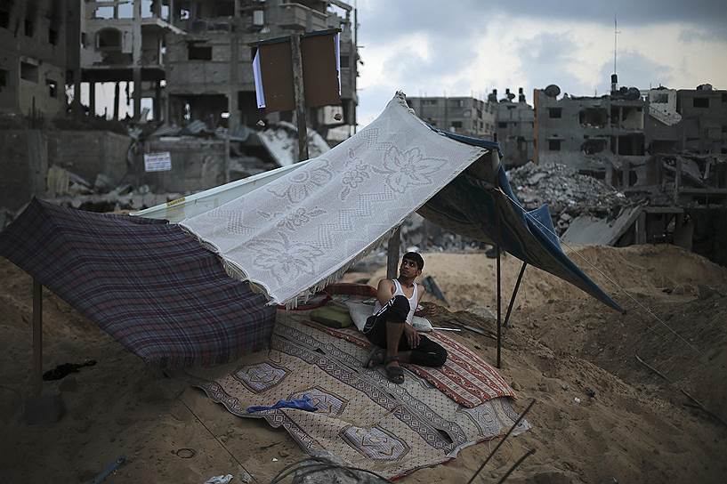 Палестинец во временной палатке возле своего разрушенного дома в Газе