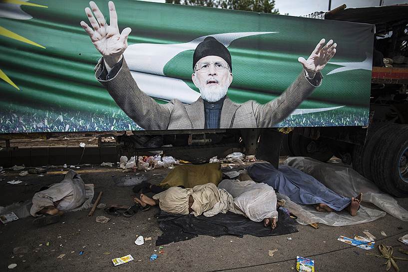 Сторонники пакистанской оппозиции спят под грузовиком с постером их лидера — суфийского богослова Тахира Кадри — во время Марша революции в Исламабаде