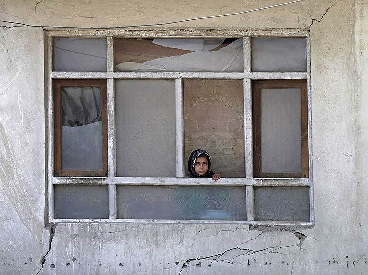 Афганская девочка выглядывает из окна, выбитого взрывной волной при атаке террориста-смертника на КПП возле аэропорта в Кабуле