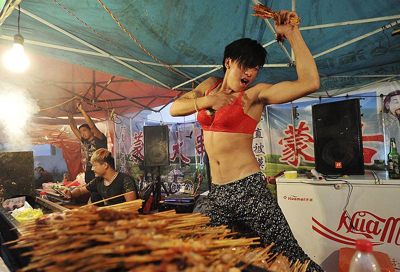 Продавец кебабов на рынке в китайском Юнкане танцует, чтобы привлечь покупателей
