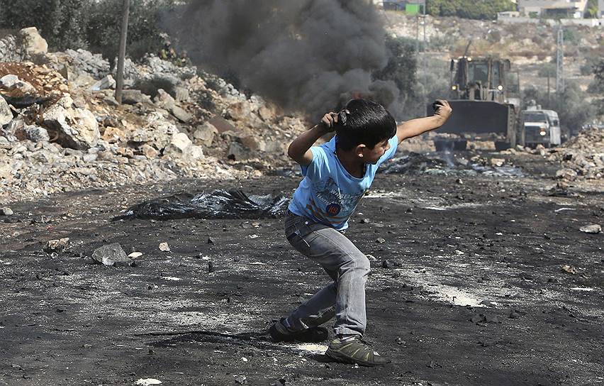 Юный палестинец кидает камни в израильских солдат во время протестов в поселении Кофр-Кадом на Западном берегу реки Иордан