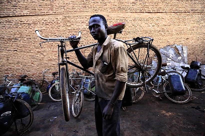 Местный житель с велосипедом через плечо доставляет нефть в Хартуме (Судан)