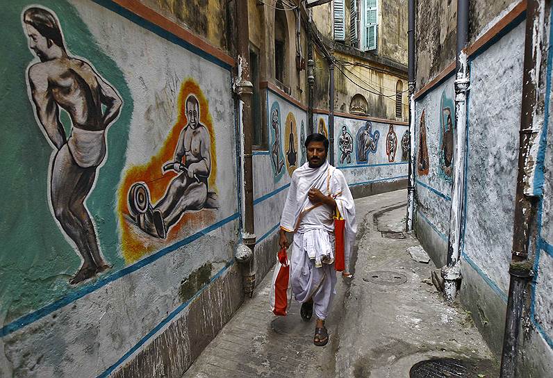 Калькутта, Индия. Мужчина на улице, украшенной изображениями традиционной индийской борьбы