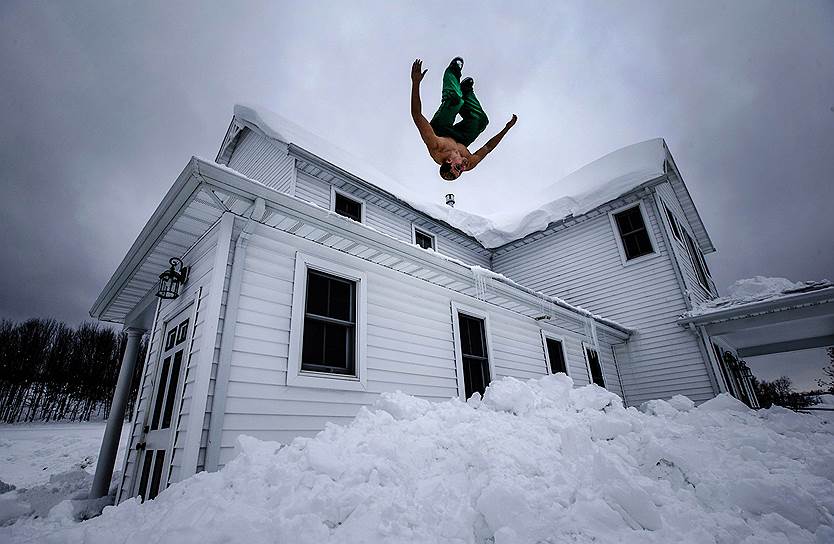 Коулсвилл, штат Нью-Йорк, США. Местный житель прыгает в снег после очистки крыши