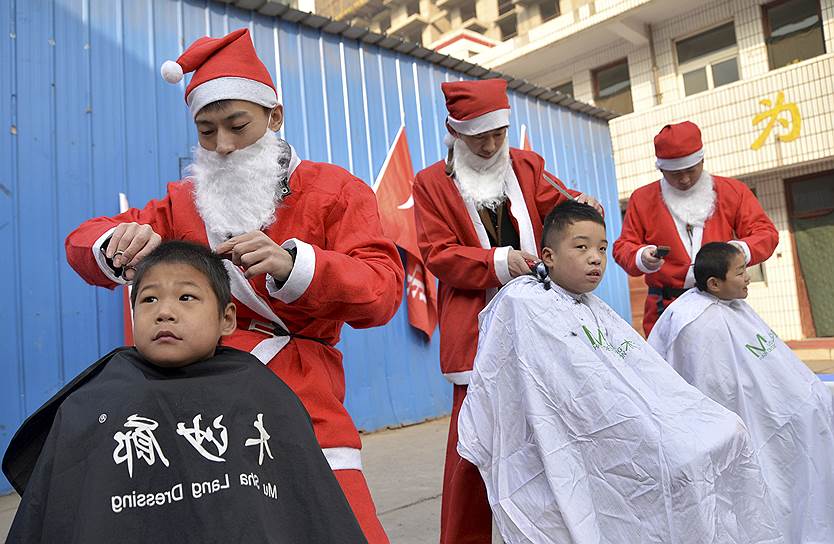 Ханьдань, провинция Хэбэй, Китай. Волонтеры, одетые в костюмы Санта-Клаусов, стригут детей из бедных семей