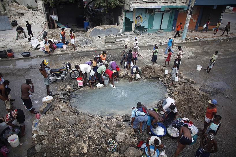 На фото: жители Порт-о-Пренса набирают воду из сломанной трубы возле президентского дворца
