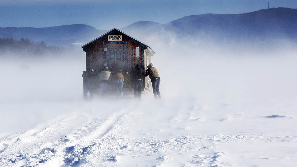 Мередит, США. Рыбаки толкают передвижной дом по замерзшему озеру во время снежной бури