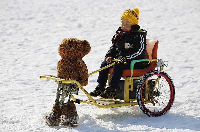 Пекин, Китай. Мальчик катается на повозке, которую тянет робот в костюме мишки Тедди, во время фестиваля льда и снега 