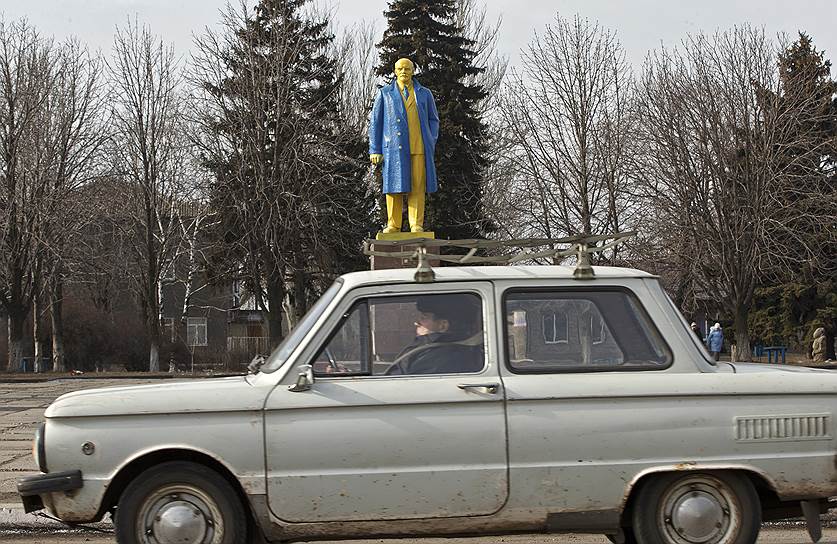 Великая Новоселка, Донецкая область, Украина. Мужчина за рулем на фоне памятника Владимиру Ленину, выкрашенного в цвета украинского флага