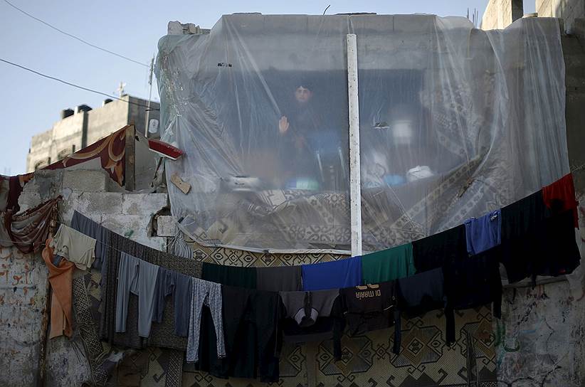 Бейт-Ханун, северная часть сектора Газа. Мальчик смотрит через занавеску, которая заменяет окно дома, разрушенного в результате обстрела