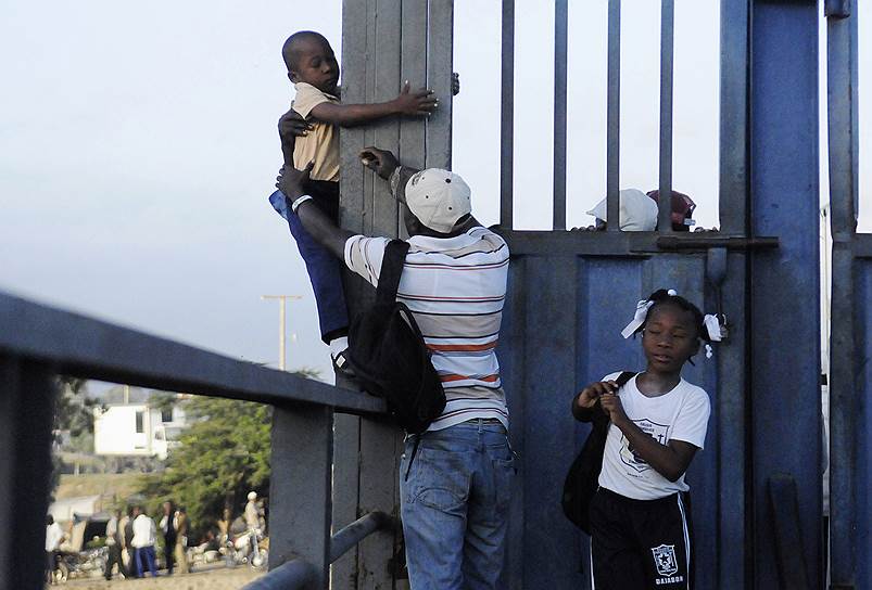 Отец помогает сыну перелезть через закрытый мост, который разделяет Гаити и Доминиканскую республику, где находится его школа