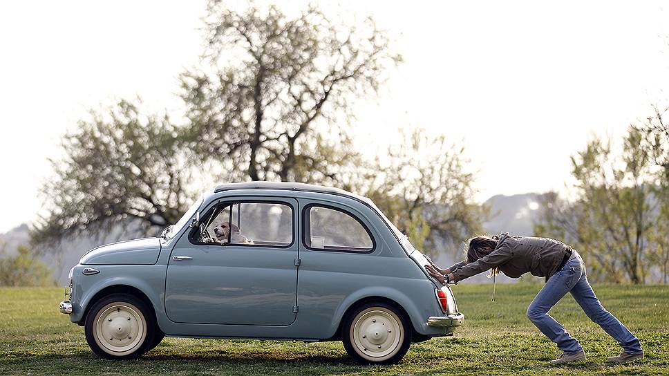 Рим, Италия. Женщина толкает свой Fiat 500, в то время как ее собака сидит на водительском сиденье