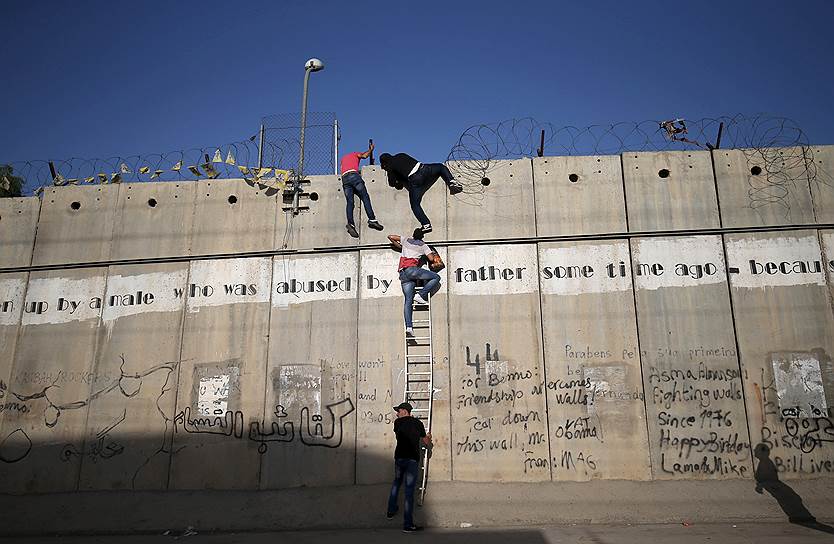 Аль-Рам, Палестина. Палестинцы, которым был запрещен въезд на территорию Иерусалима из-за возрастных ограничений, перелезают через забор, разделяющий два государства, чтобы принять участие в пятничной молитве в мечети аль-Акса