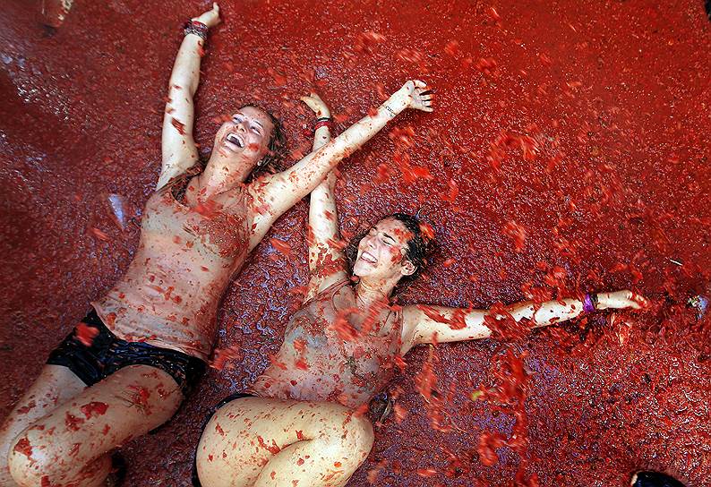 Валенсия, Испания. Девушки лежат в луже раздавленных помидоров во время ежегодного таматного боя «Томатина»