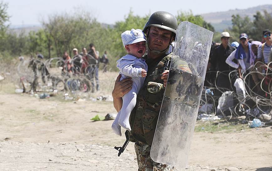 Гевгелия, Македония. Полицейский держит ребенка на руках в безопасности в то время, как мигранты пытаются пересечь македонскую границу 