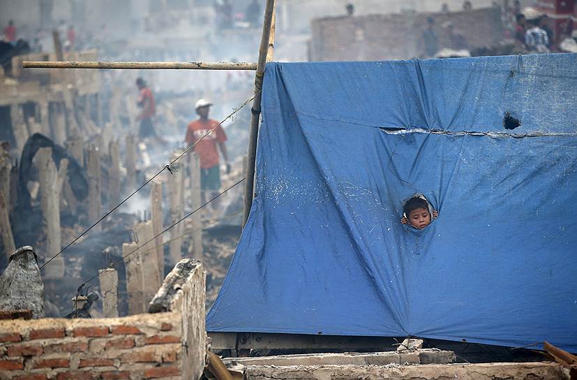 Джакарта, Индия. Мальчик выглядывает из дырки в ткани временного убежища одной из семей, оставшихся без крыши над головой из-а пожара, уничтожившего сотни домов в трущобном районе Капук-Райа