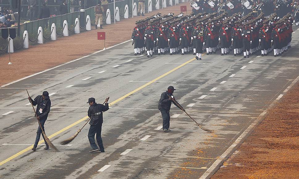 Нью-Дели, Индия. Уборщики, подметающие дорогу перед строем солдат, марширующих во время парада в честь Дня республики 