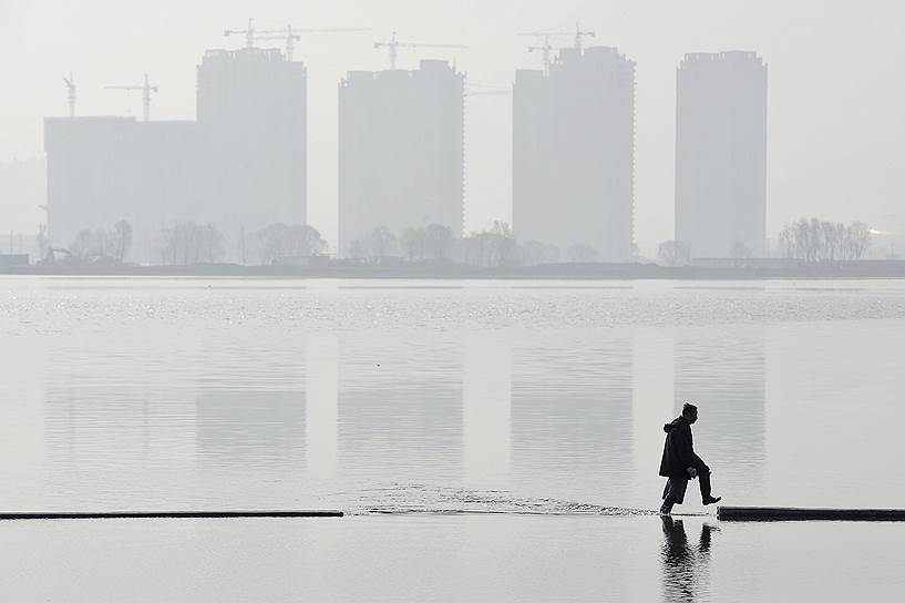 Тайюань, Китай. Мужчина идет по искусственному озеру в строящемся спальном районе