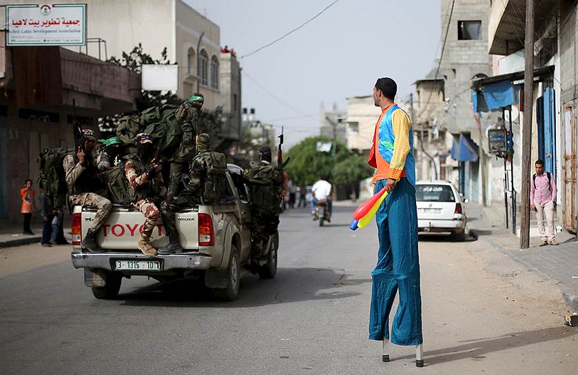 Сектор Газа. Палестинец на ходулях смотрит на боевиков ХАМАС, которые едут  на пикапе по улице в северной части сектора Газа 