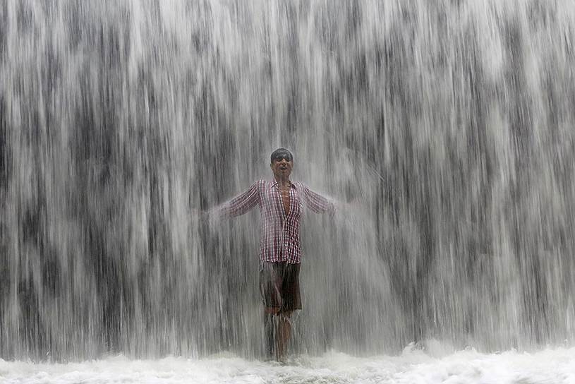 Мумбай, Индия. Мальчик стоит под потоком воды, переливающейся через плотину после сильного ливня  