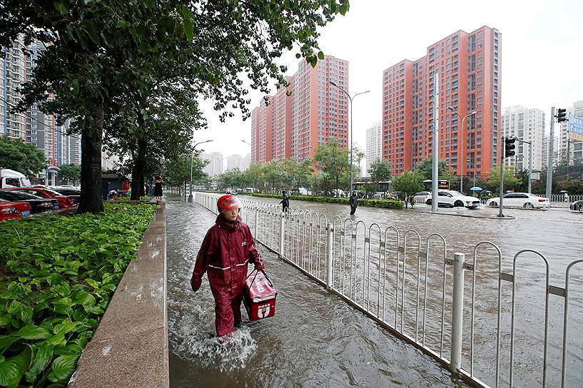 Пекин, Китай. Курьер, доставляющий еду, на затопленной улице