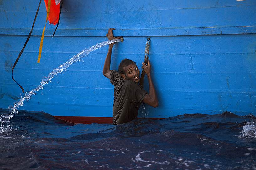Сабрата, Ливия. Мужчина пытается удержаться за лодку во время операции по спасению мигрантов в Средиземном море