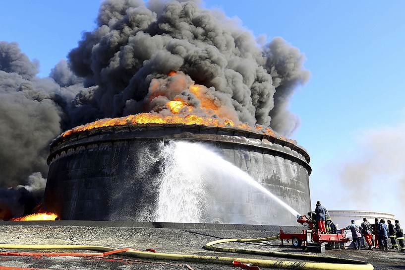 Пожарные тушат горящий нефтяной резервуар в ливийском Рас-Лануфе. Боевики ИГ обстреляли этот порт