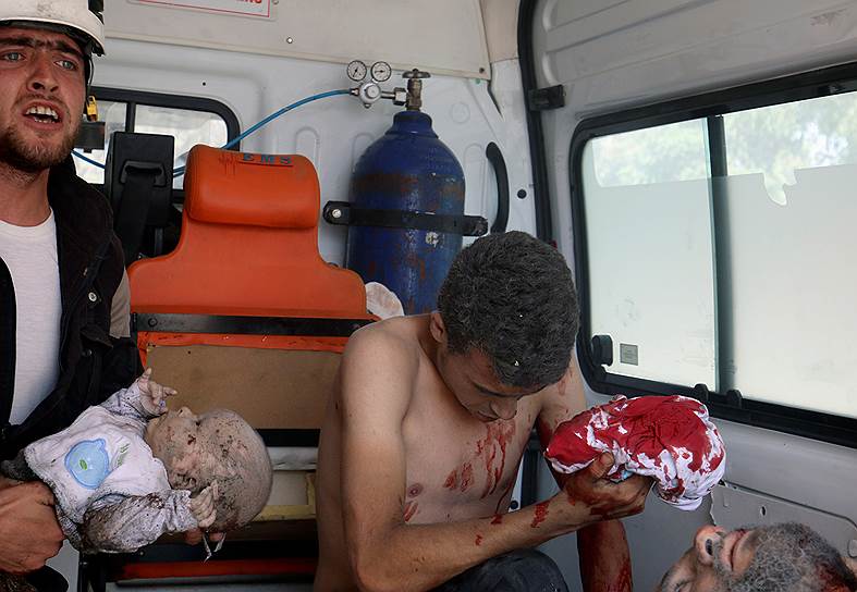Член «Сирийской гражданской обороны» держит раненого младенца в машине скорой помощи после того, как ребенка вытащили из-под завалов в пригороде Алеппо