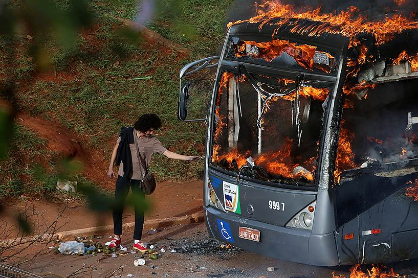 Бразилиа, Бразилия. Мужчина поджигает сигарету о горящий автобус, который был подожжен во время демонстраций против конституционной реформы