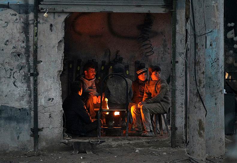 Алеппо, Сирия. Местные жители греются у огня в здании, где раньше находился магазин