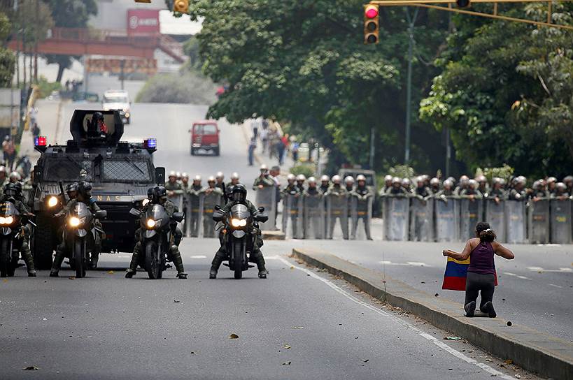 Каракас, Венесуэла. Участник «Марша маршей» стоит на коленях перед приближающейся колонной полицейских