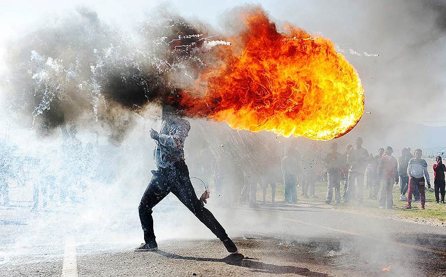 Фандулвази Джайкло, ЮАР. Протесты в г. Грабу (ЮАР) &lt;br>

Освоение территории и нехватка жилья привели к ожесточенным протестам в городе Грабу недалеко от Кейптауна. В ходе стычек с полицией жители устроили пожар в Департаменте дорожного движения и блокировали магистраль. Человек на фотографии размахивает горящей покрышкой, пытаясь остановить приближение полиции