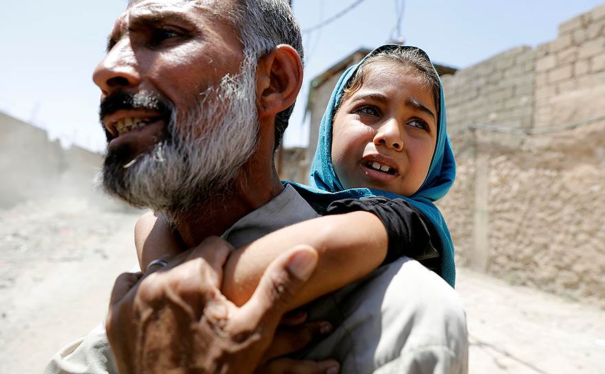 Мосул, Ирак. Мужчина с дочерью на спине убегают из дома после начала боевых действий между вооруженными силами Ирака и боевиками «Исламского государства»